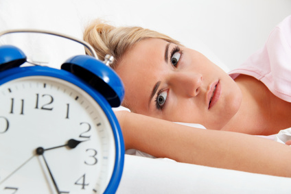 Frau mit Schlafstörungen blickt auf blauen Wecker